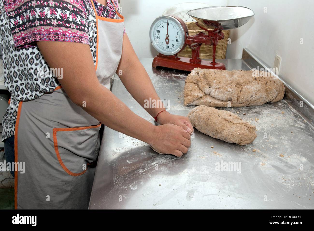 Primo piano del pugno di un fornaio che toglie l'impasto del pane integrale con le noci su un tavolo di metallo Foto Stock