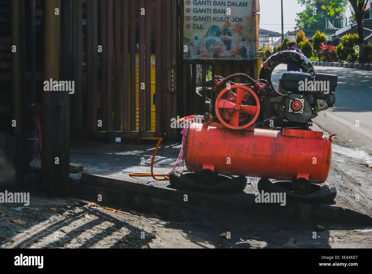 Un motore portatile per compressori d'aria arancione si trova all'esterno di una tradizionale officina stradale in Indonesia. Foto Stock