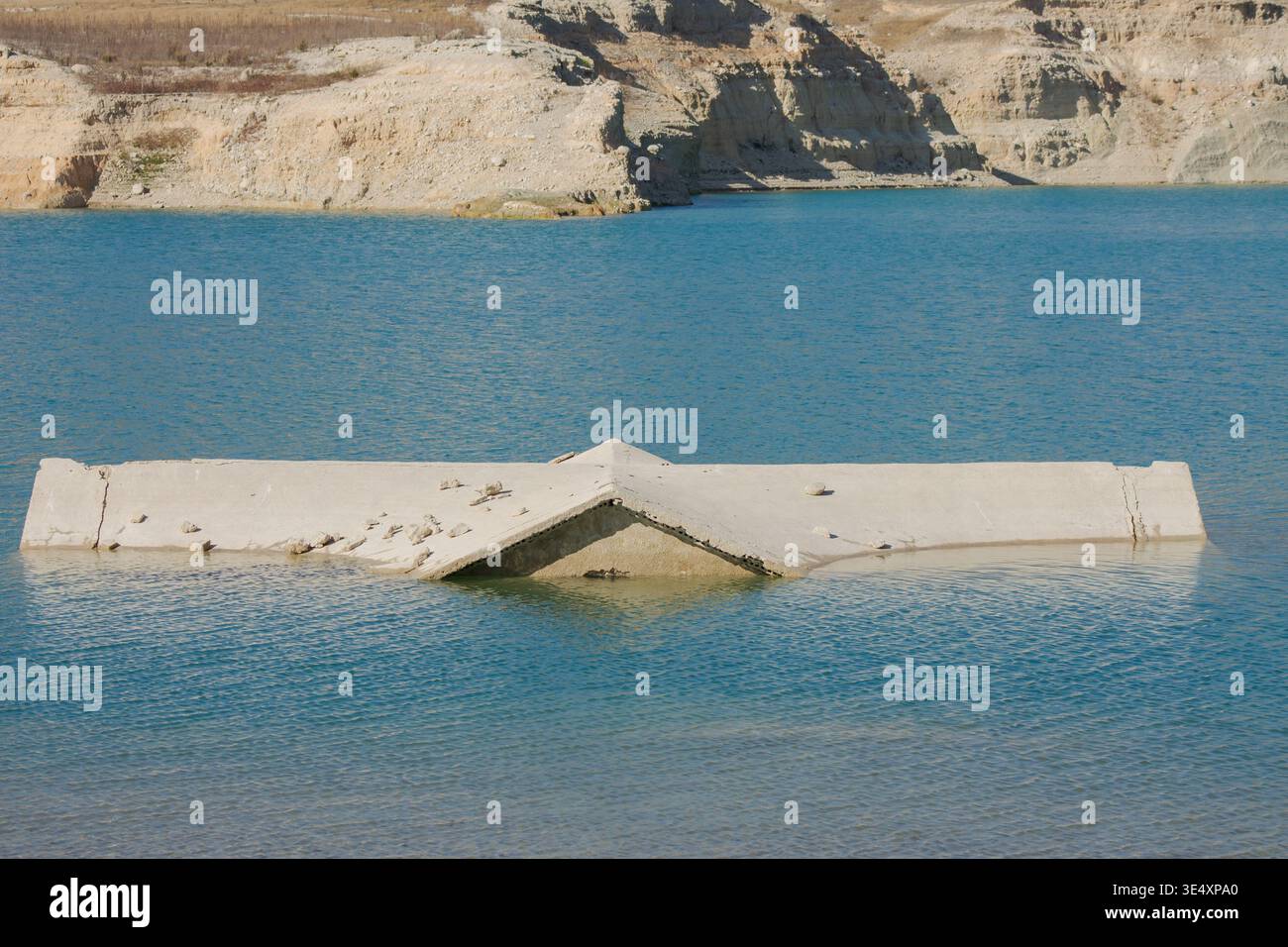 Una vista più ravvicinata di una casa sul tetto in cemento parzialmente sommersa dalle acque cristalline turchesi di un lago di cava. La struttura mostra segni di tempo Foto Stock