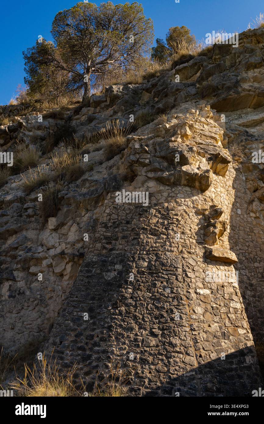 Un massiccio muro di pietra costruito direttamente in una scogliera calcarea presso il bacino idrico Amadorio di Alicante. Spagna. Le tradizionali caratteristiche in pietra Foto Stock