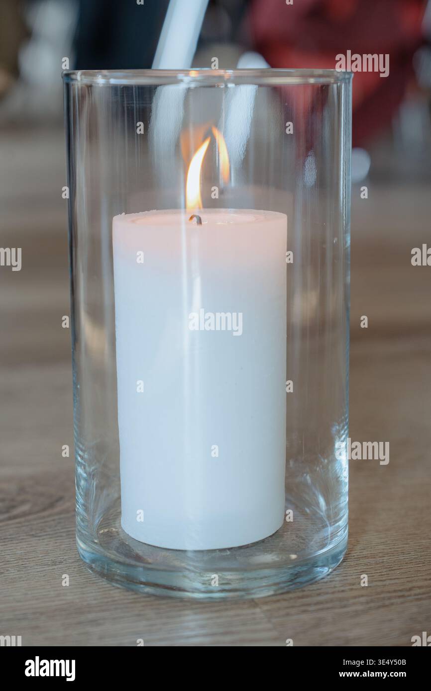 Candela minima nel supporto in vetro su pavimento in legno. Elegante elemento decorativo per interni di matrimoni, cerimonie o eventi. Illuminazione tranquilla e suggestiva. Foto Stock