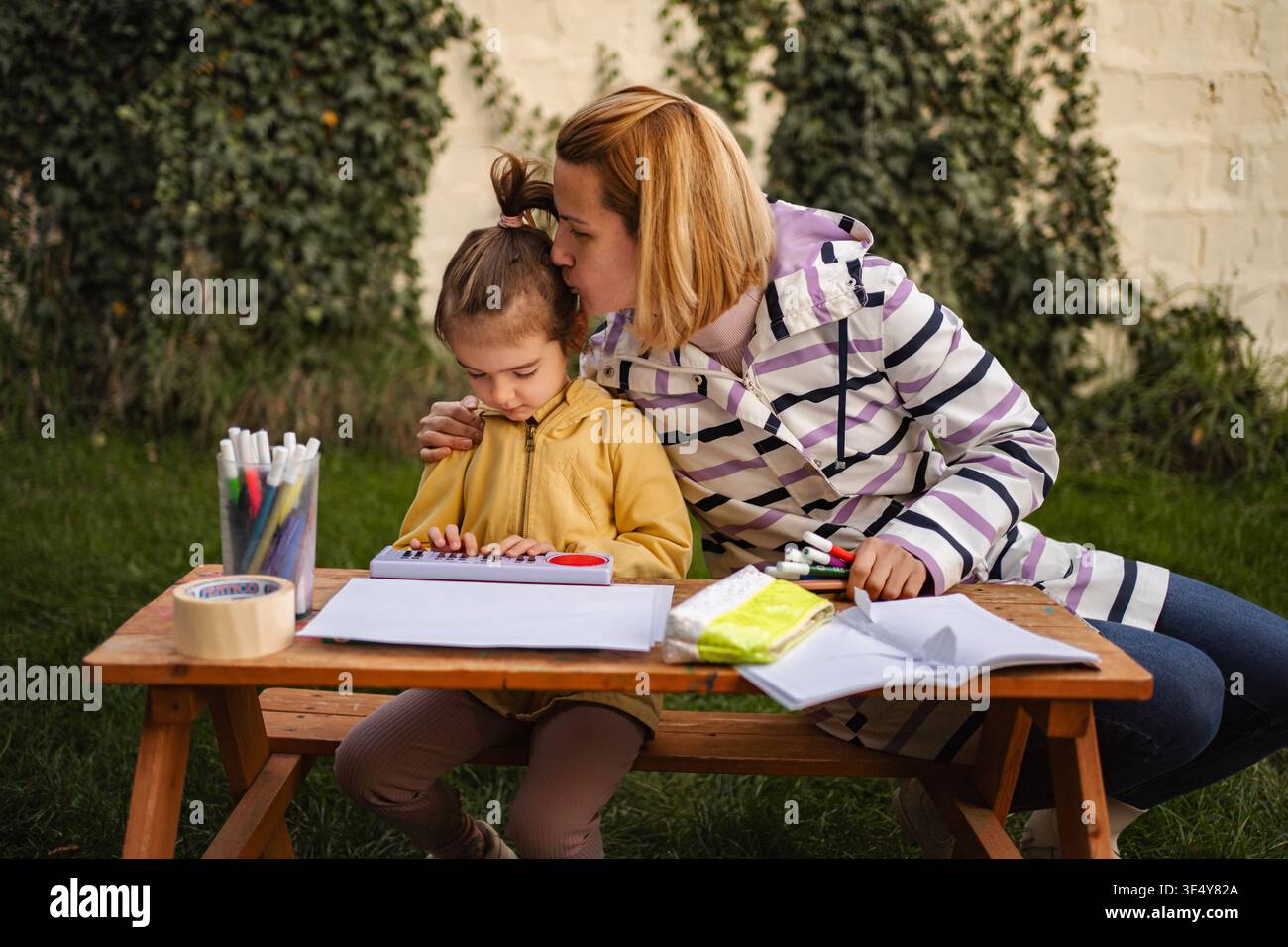 Madre che bacia la figlia che impara la tastiera all'aperto durante il periodo scolastico Foto Stock