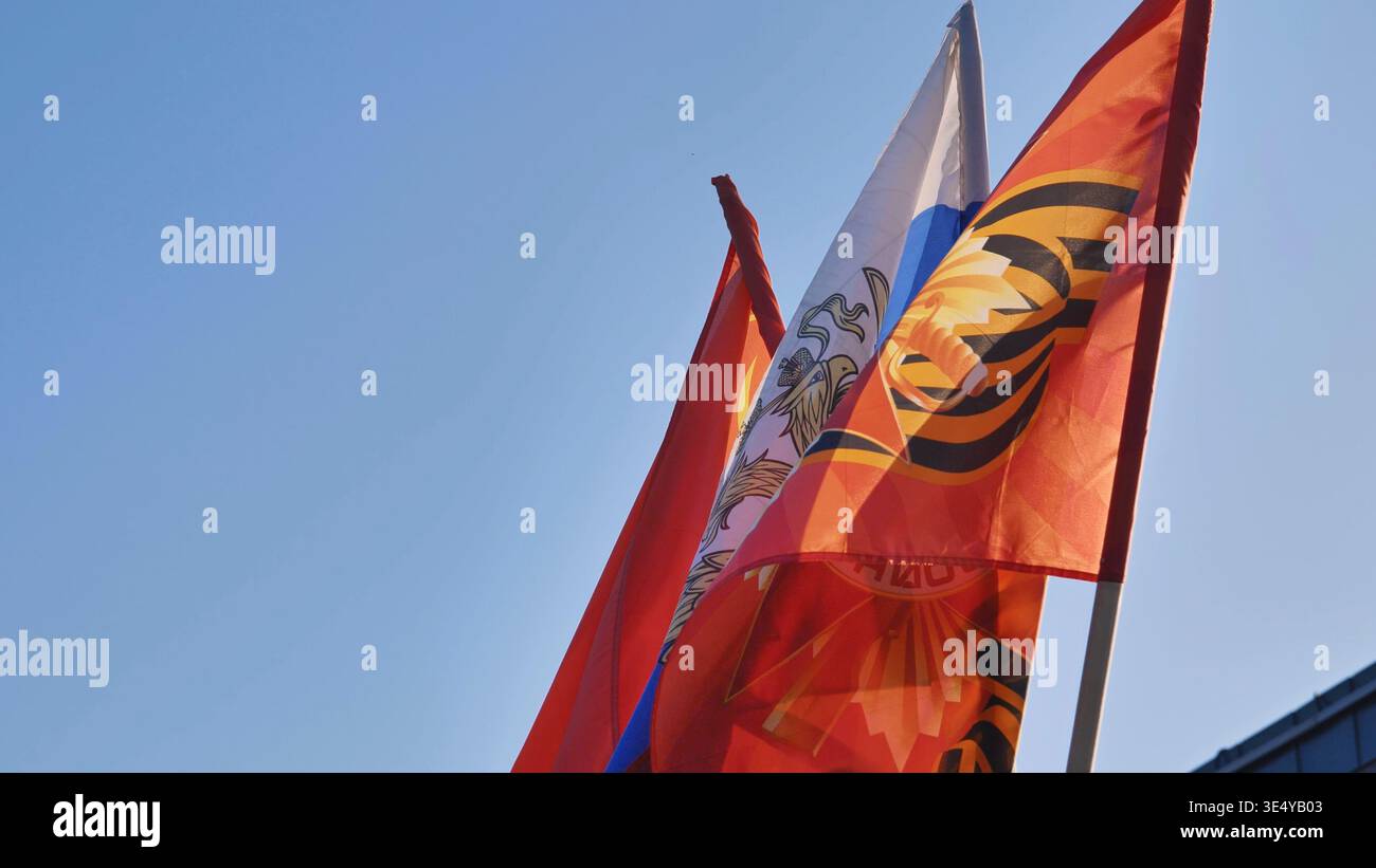 Bandiere nazionali russe e del nastro di San Giorgio che battono simboli patriottici contro il cielo blu Foto Stock