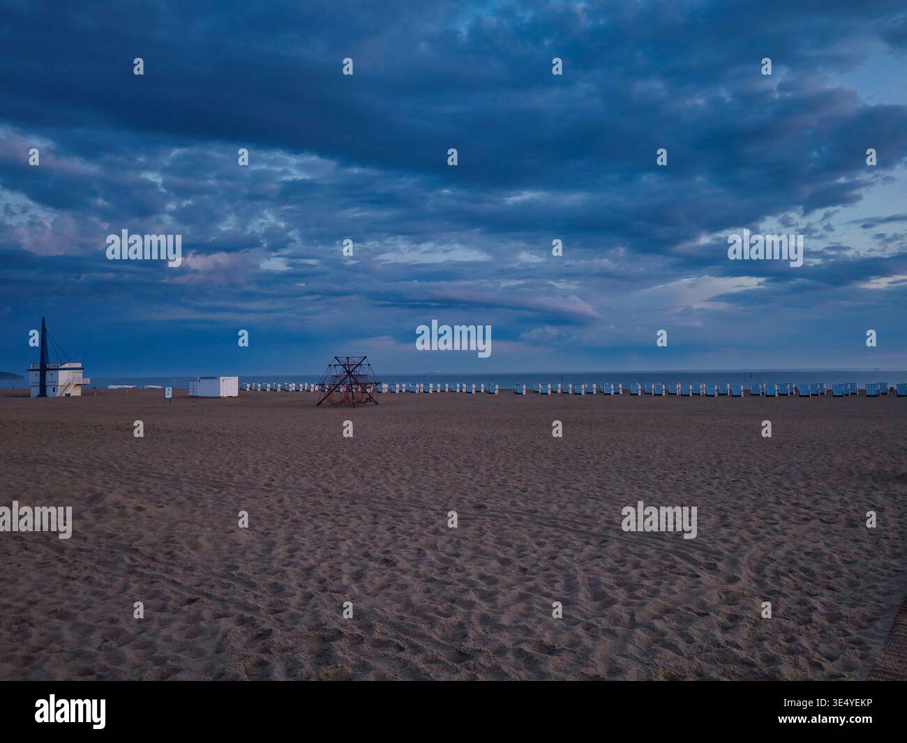 Einsamer Sandstrand in Warnemünde zur blauen Stunde: Weite Sicht über den leeren Strand und die Ostsee unter einem dramatischen Wolkenhimmel Foto Stock