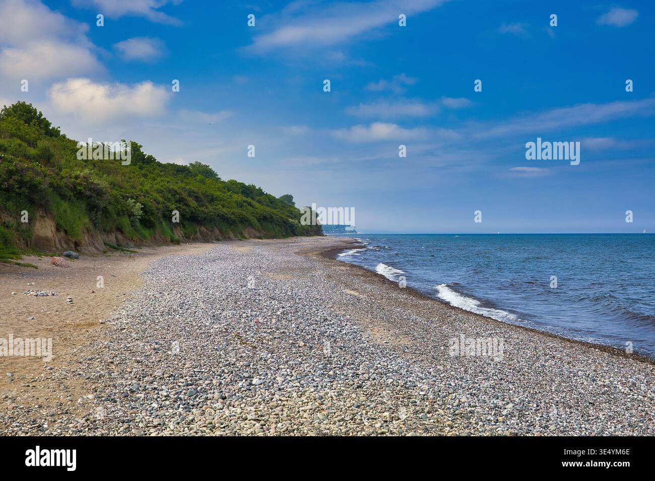 Naturbelassener Steinstrand an der Ostseeküste unter bewölktem Himmel – Weite Meereslandschaft mit Küstenvegetation und fernen Spaziergängern Foto Stock