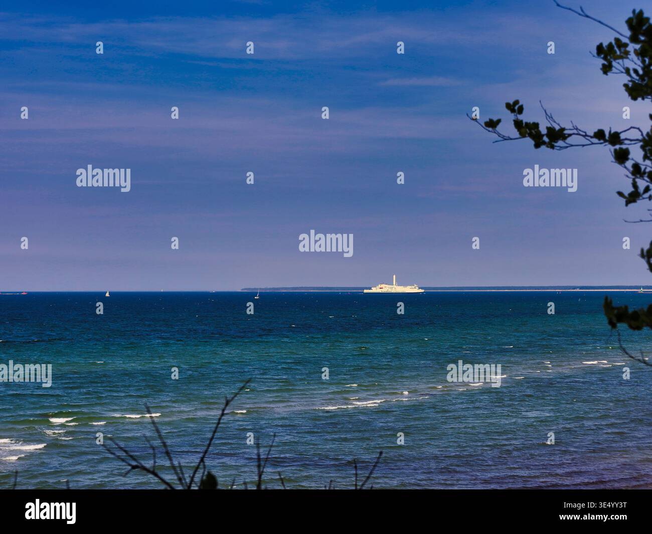 Blick durch Bäume auf ein Frachtschiff am Horizont der blauen Ostsee vor der Küste von Mecklenburg-Vorpommern Foto Stock