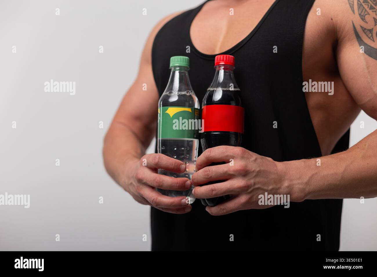 Uomo sano muscolare atletico che tiene due bibite dolci cola in bottiglia di plastica. Salute e bevande Foto Stock