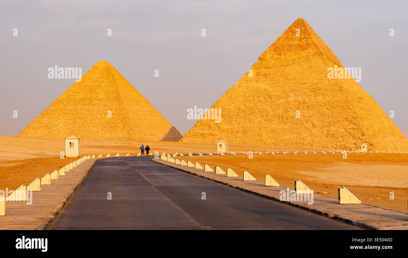 Due piramidi di Giza con strada asfaltata e due persone che camminano a Giza, il Cairo, in Egitto Foto Stock