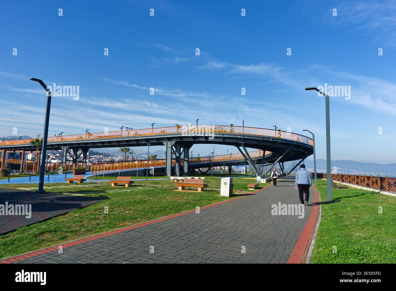 Una vista di vita dei cittadini che utilizza un moderno ponte pedonale a spirale in un parco sul mare, evidenziando la mobilità urbana e le infrastrutture pubbliche. Foto Stock
