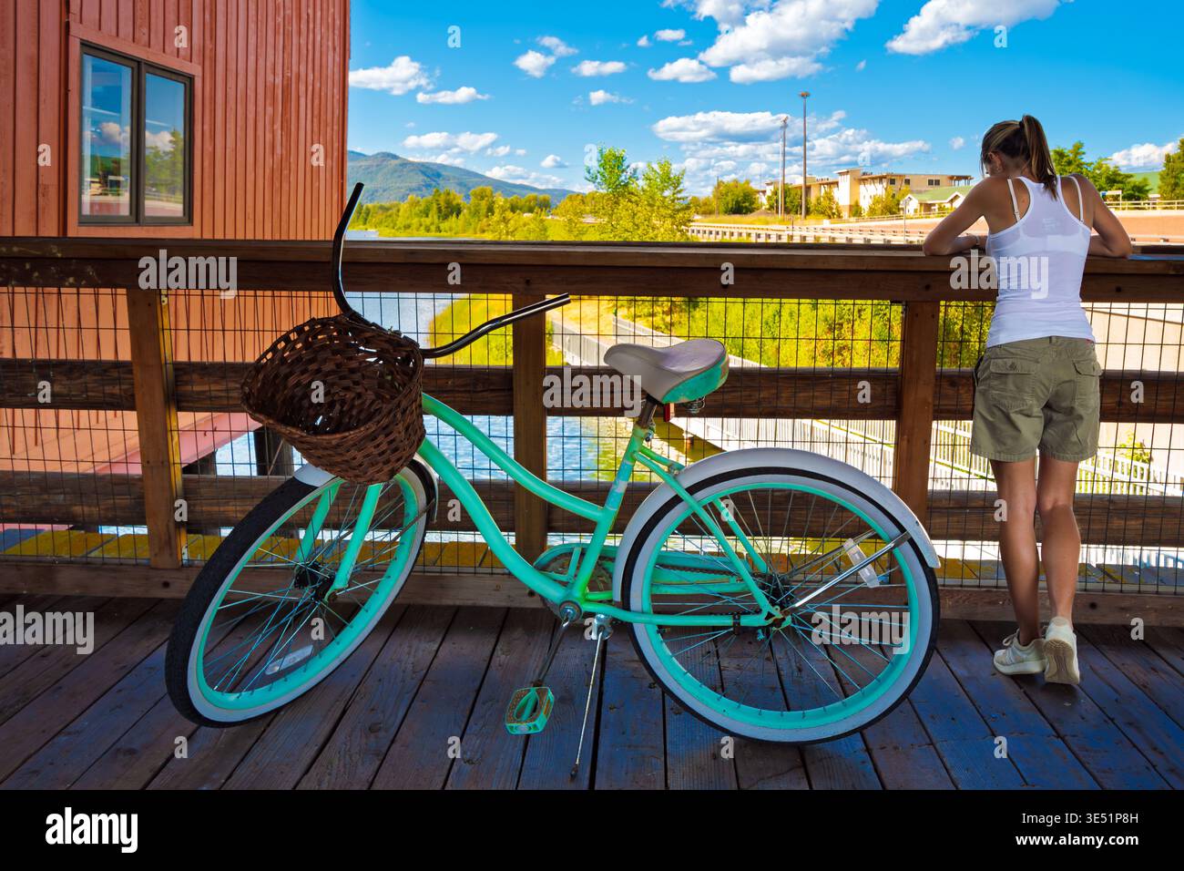 Una giovane donna con una bicicletta turchese si ferma lungo il Cedar Street Bridge sopra il lago Pend Oreille Sand Creek nella piccola città di Sandpoint, Idaho. Foto Stock