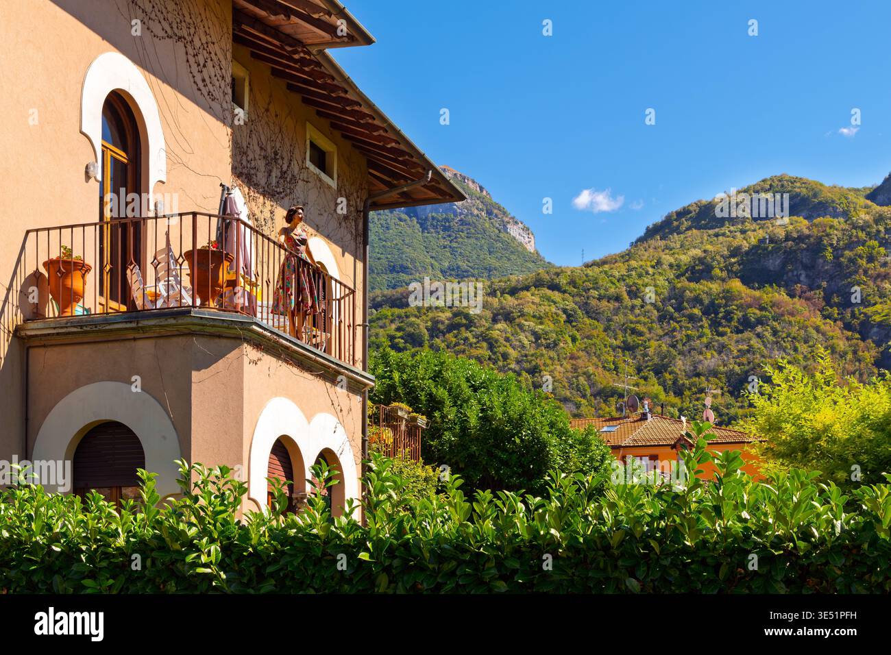 Una donna italiana si erge su una terrazza balcone di una villa che guarda alle montagne in una giornata di sole a Menaggio, in Italia, sulle rive del Lago di Como. Foto Stock