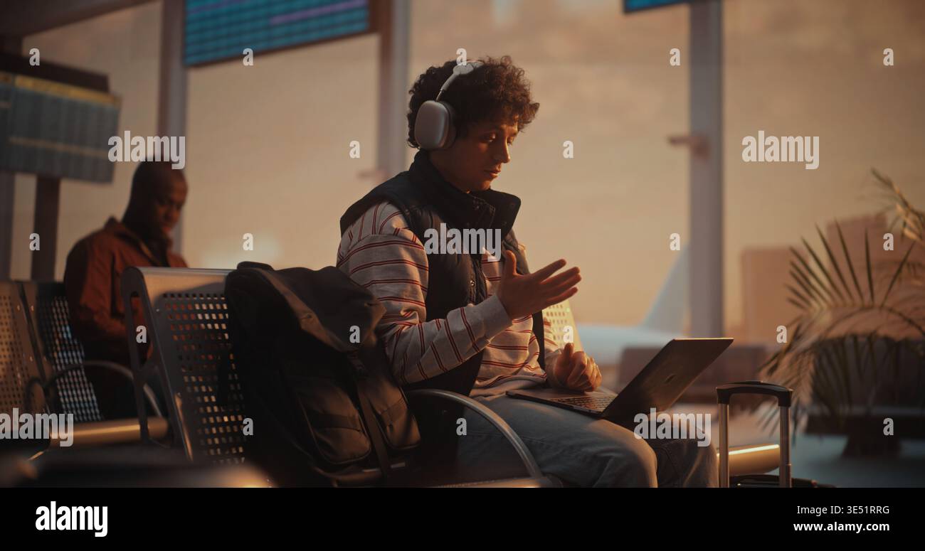 Giovane professionista che effettua una videochiamata aziendale all'aeroporto con l'aereo in partenza alle spalle. Giovane uomo con capelli ricci partecipa a importanti riunioni di lavoro tramite laptop. Concetto di comunicazione globale. Foto Stock