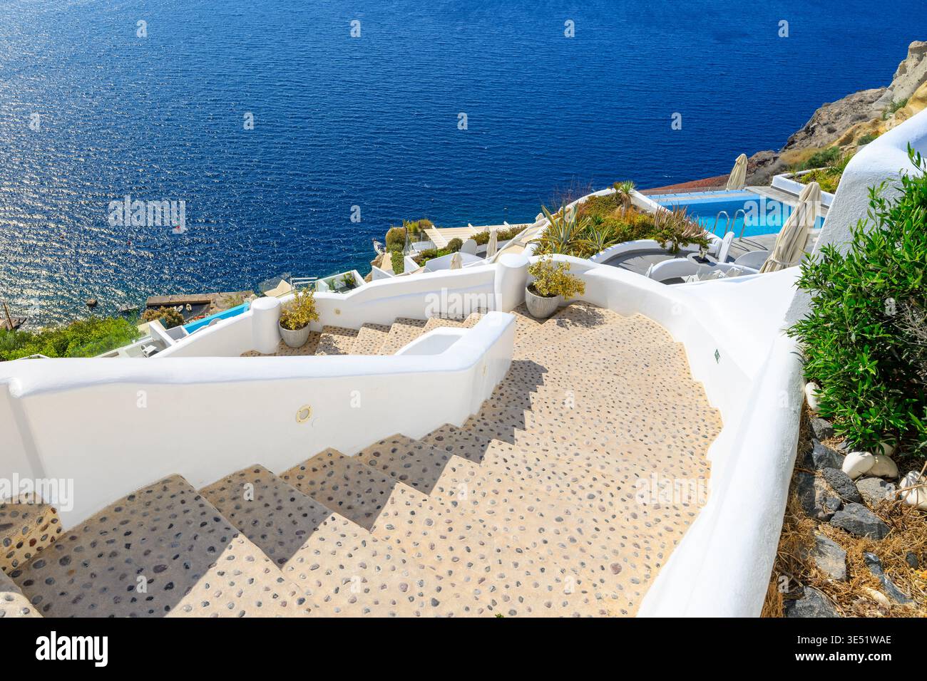 Una ripida scala si snoda verso il basso verso terrazze imbiancate a calce con resort e piscine nel villaggio di Oia, in Grecia, sull'isola greca di Santorini. Foto Stock