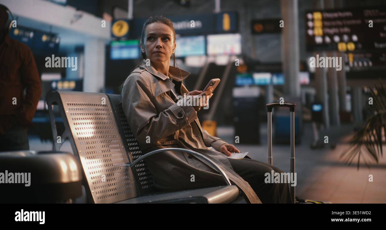 Viaggiatore femminile che confronta il biglietto digitale con il tabellone informativo dell'aeroporto. La donna guarda attentamente la tavola di volo in alto, il numero del gate di riferimento incrociato e l'orario di partenza con i dati sullo schermo. Foto Stock