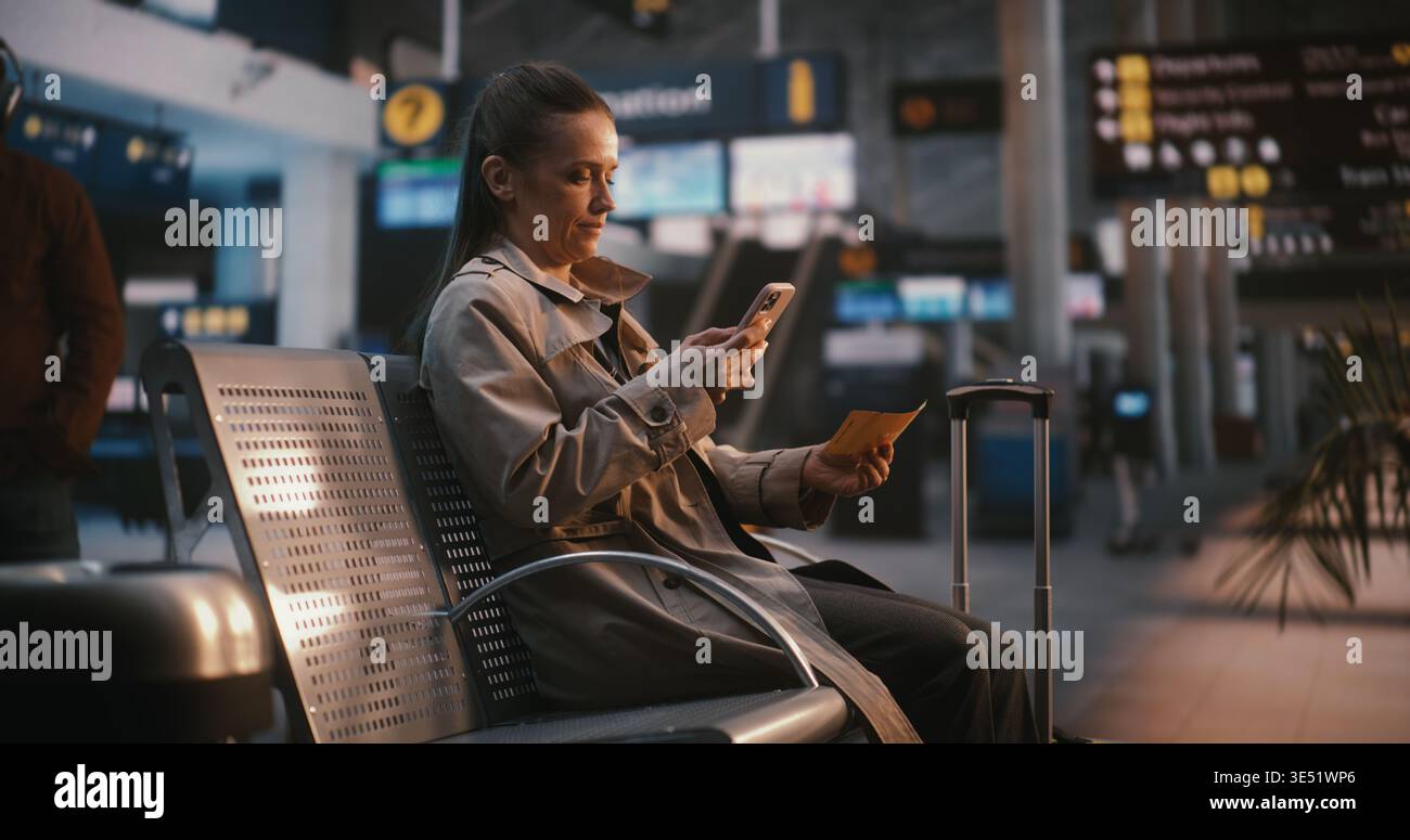 Viaggiatore femminile che confronta il biglietto digitale con il tabellone informativo dell'aeroporto. La donna guarda attentamente la tavola di volo in alto, il numero del gate di riferimento incrociato e l'orario di partenza con i dati sullo schermo. Foto Stock