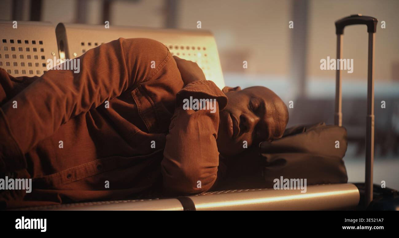 Esausto aspettando che Flight Man dorma sulle sedie dell'aeroporto. In un momento tranquillo nell'affollato terminal internazionale, il ragazzo afroamericano trova il modo di riposare su sedute dure. Concetto di stile di vita dei viaggiatori. Foto Stock