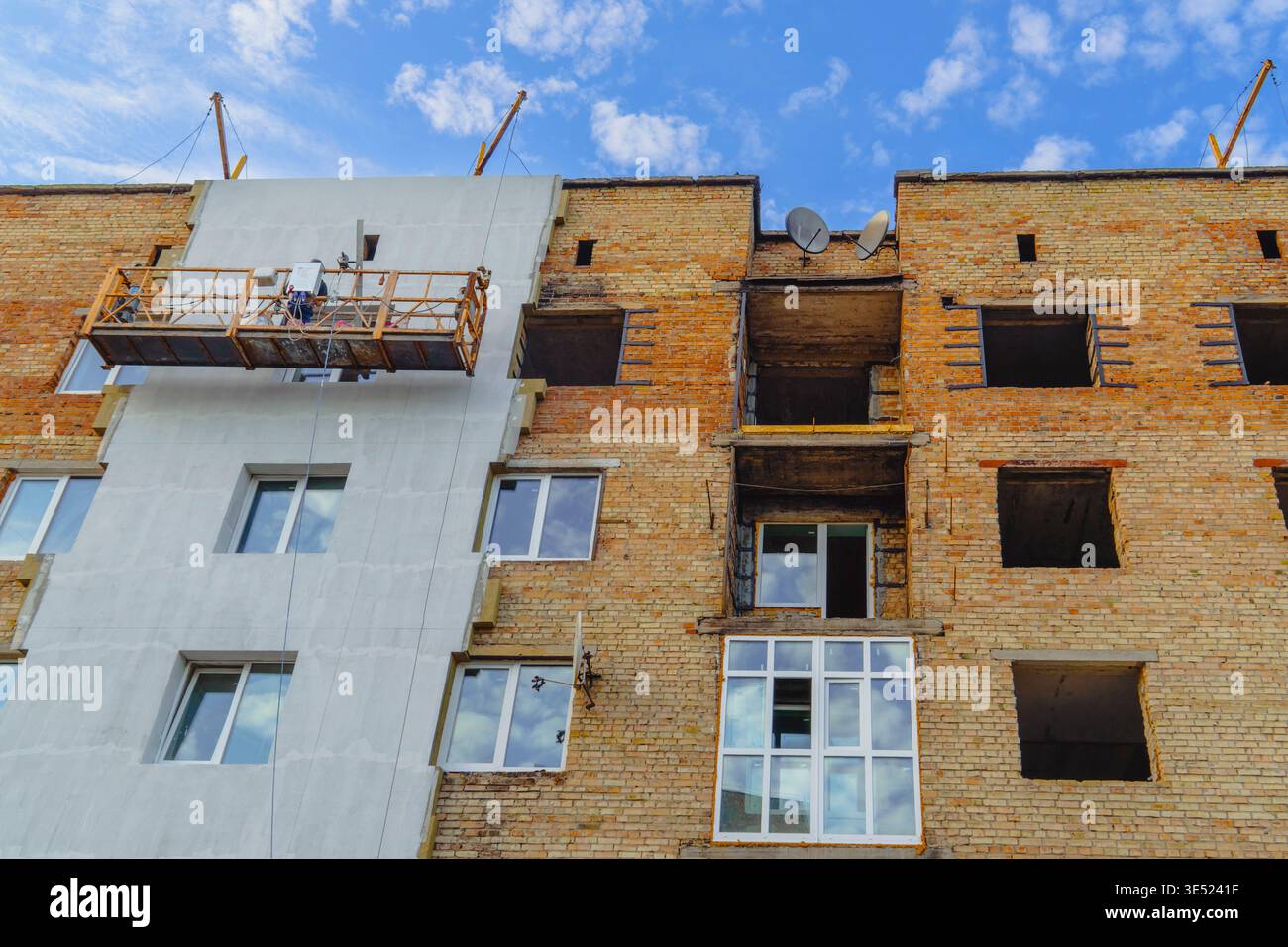 Una culla vuota è appesa a un edificio di mattoni danneggiato dalla guerra, parte della facciata è stata isolata di recente e sono state installate finestre Foto Stock