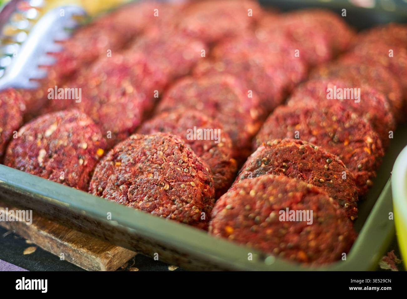 Vista ravvicinata di più polpette di carne cruda disposte in file ordinate all'interno di un vassoio rettangolare in metallo o plastica Le polpette sono rotonde, rossastre dentro Foto Stock