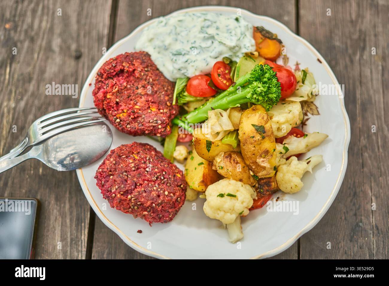 Un piatto di ceramica bianca pieno di un colorato pasto vegetariano siede su un rustico tavolo di legno. Il piatto presenta due polpettine di verdure rossastre-viola, Foto Stock