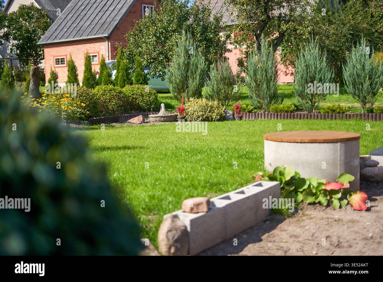 Un giardino residenziale ben mantenuto caratterizzato da un lussureggiante prato verde in primo piano e sullo sfondo. In primo piano a destra, c'è un cemento rotondo Foto Stock