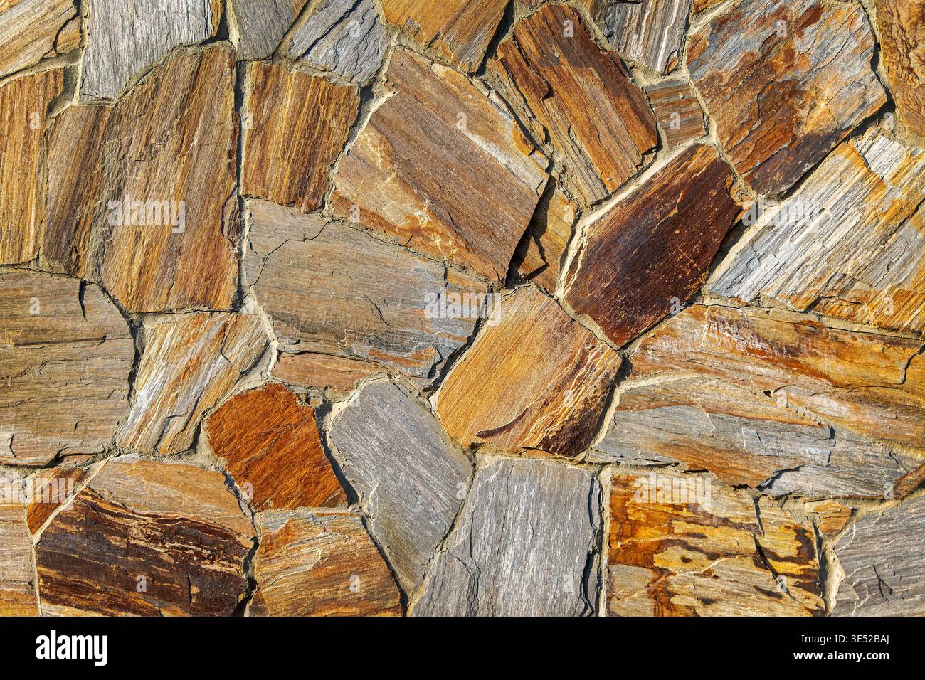 Pareti in pietra naturale dai toni caldi. Primo piano di una parete irregolare in pietra naturale con tonalità grigie e ruggine, ideale per ricerche su muratura Foto Stock