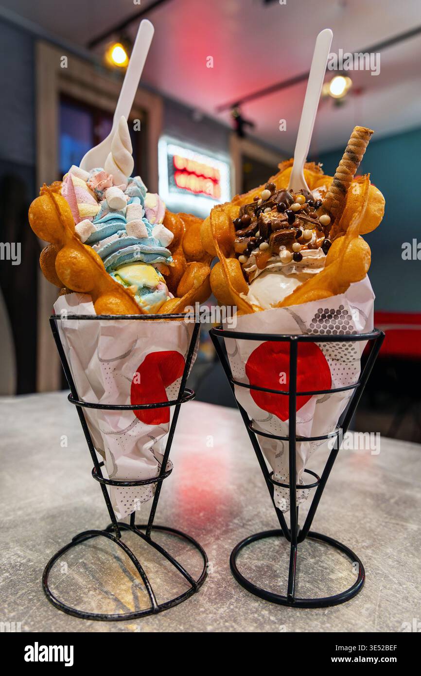 Coni di gelato Bubble waffle al Cafe. Due coni da dessert con cialde di cialde ripieni di piatti morbidi e condimenti su un tavolo da caffè, che mostrano un colorato Foto Stock
