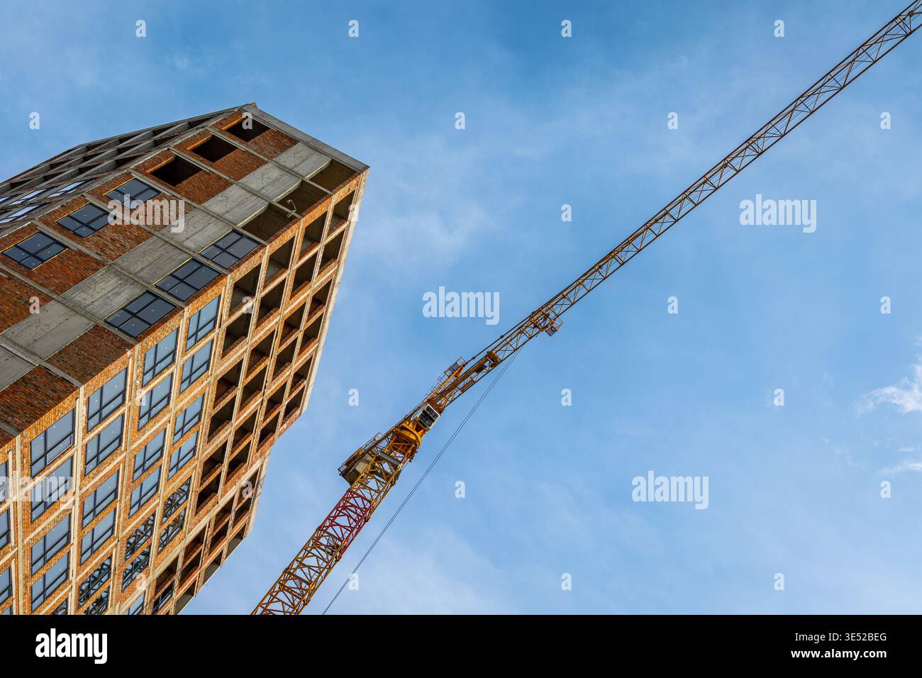Alto edificio in costruzione con gru a torre. Foto ad angolo basso di un alto edificio incompiuto con una gru a torre contro il cielo blu Foto Stock