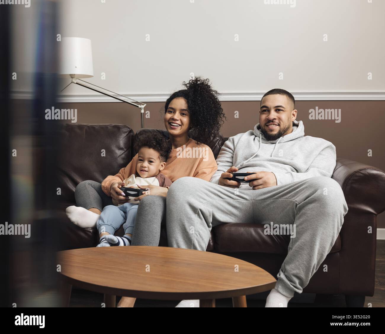 Madre, padre e figlio piccolo che giocano a videogiochi mentre si siedono sul divano a casa Foto Stock