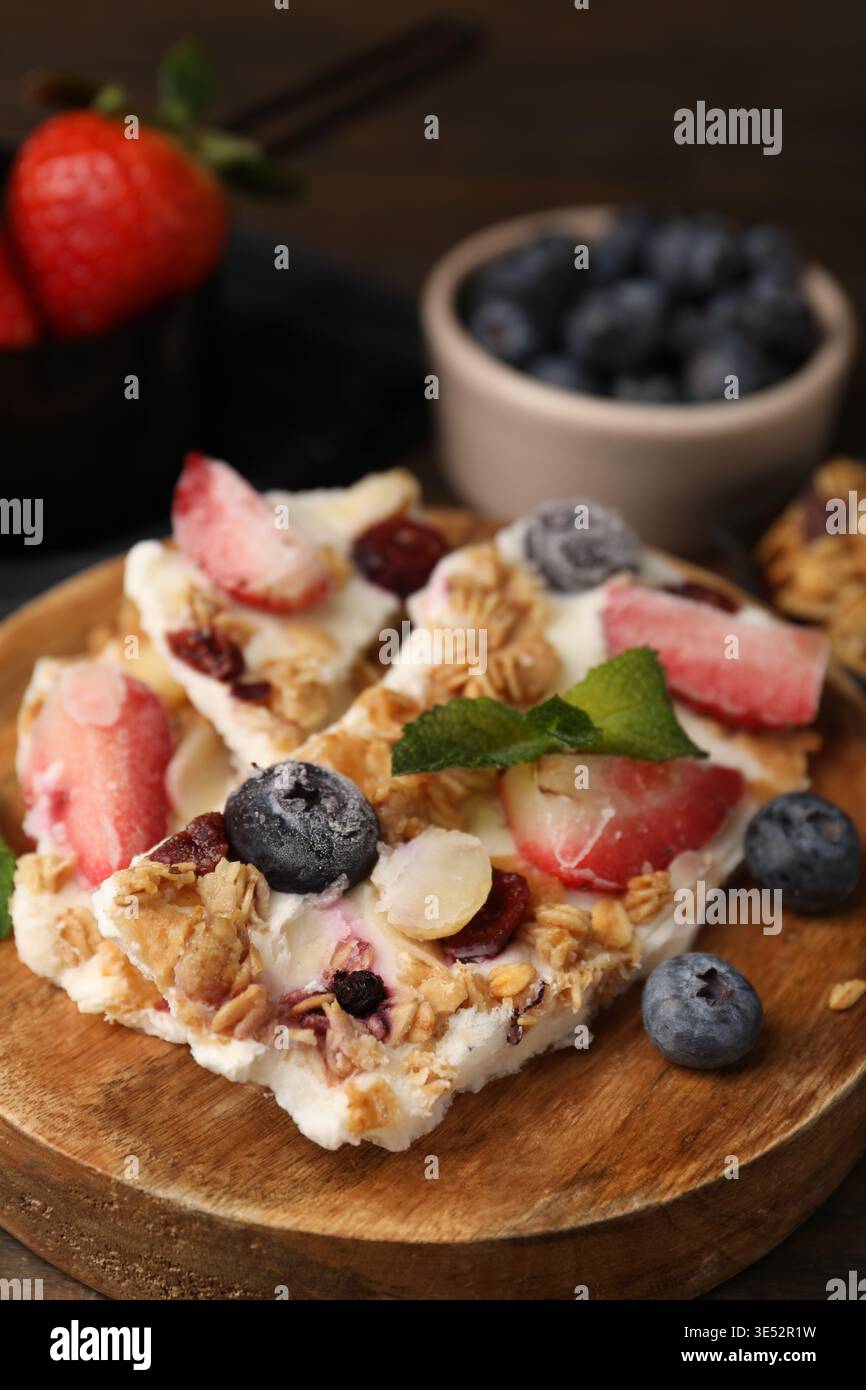 Pezzi di gustosa corteccia di yogurt con frutti di bosco, menta e muesli sul tavolo, primo piano Foto Stock