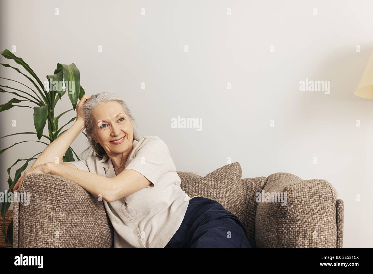 Donna anziana pensiva che si rilassa a casa seduta in una poltrona Foto Stock
