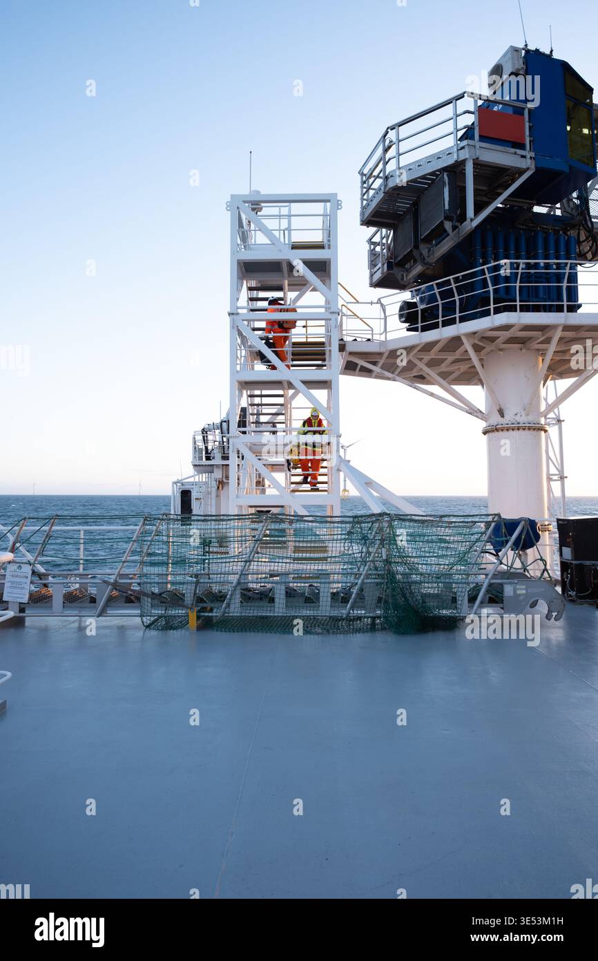 Ampia vista sul ponte di un'imbarcazione per operazioni di manutenzione che mostra i lavoratori sulle scale, il sistema di passerella e le turbine eoliche offshore all'orizzonte. Foto Stock