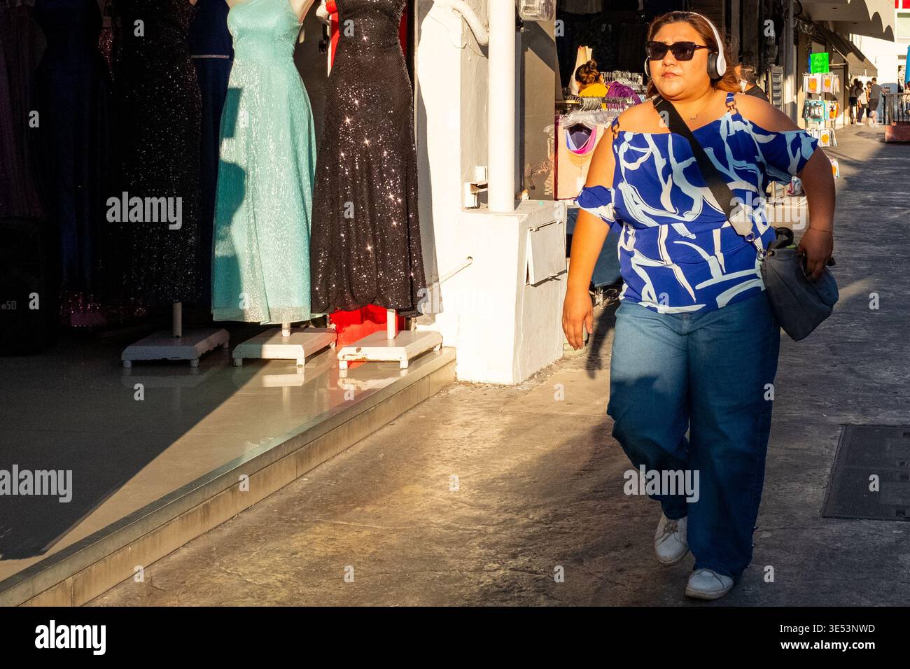Giovane donna messicana alla moda che indossa le cuffie che cammina lungo una strada pedonale a Merida, Messico Foto Stock