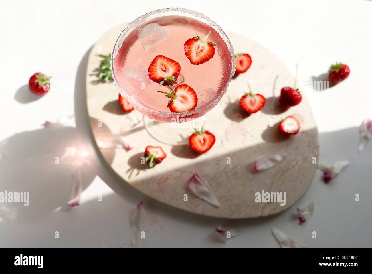 Cocktail di margarita rosa alla fragola con bordo di zucchero su vassoio di marmo Frutti di bosco appena tagliati che galleggiano in una bevanda di rose frizzanti con ombre di ghiaccio e luce solare Foto Stock