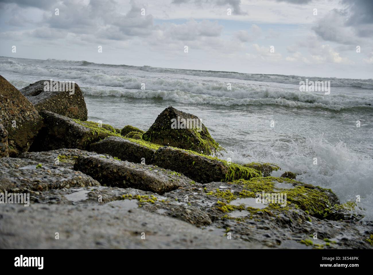 Onde che spruzzano sulla costa rocciosa ricoperte di vivaci alghe verdi Foto Stock