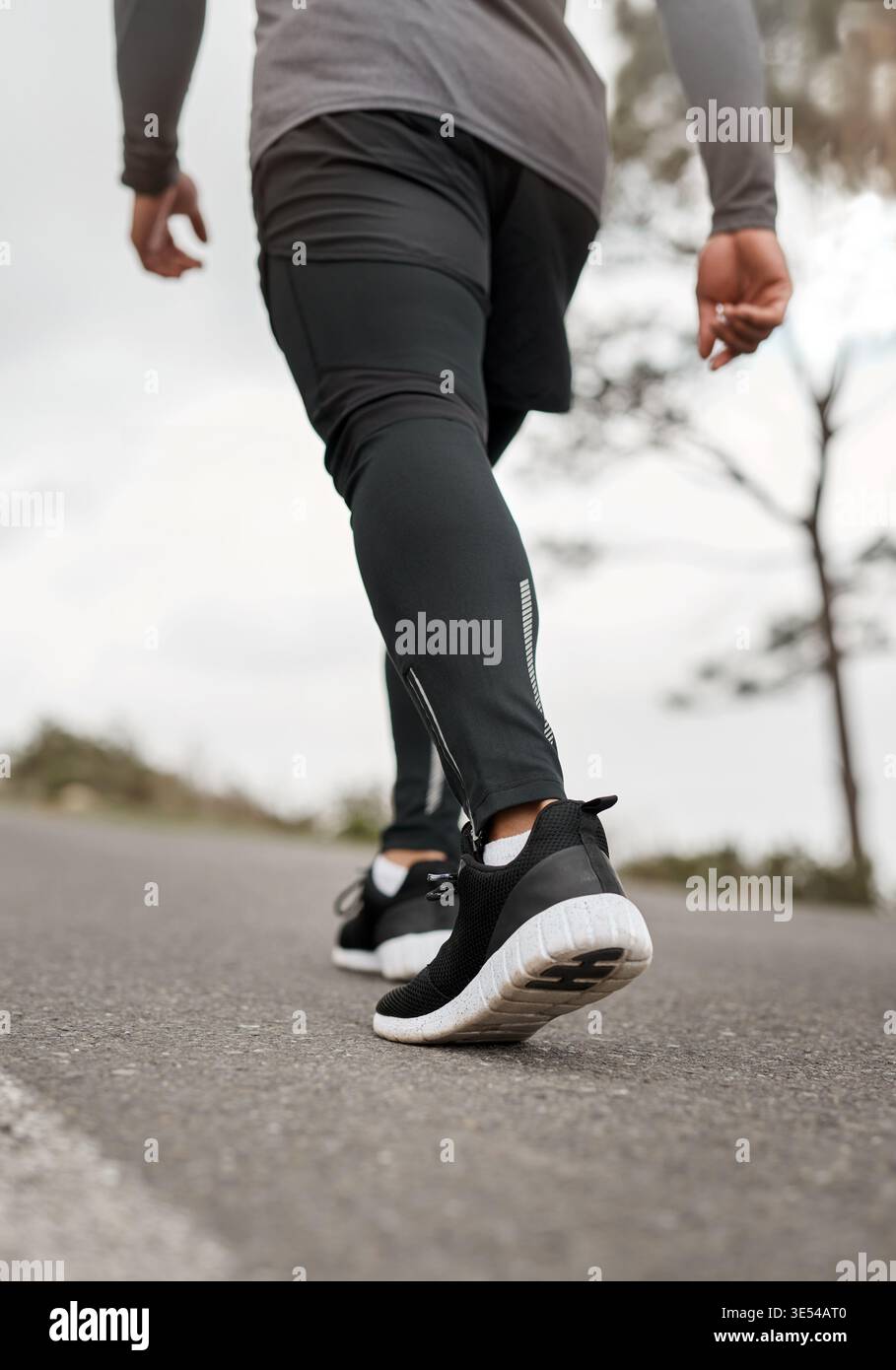 Fitness, gambe e persona su strada per l'esercizio fisico, cardio e salute con allenamento e allenamento. Angolazione ridotta, runner e attività all'aperto per lo sport Foto Stock