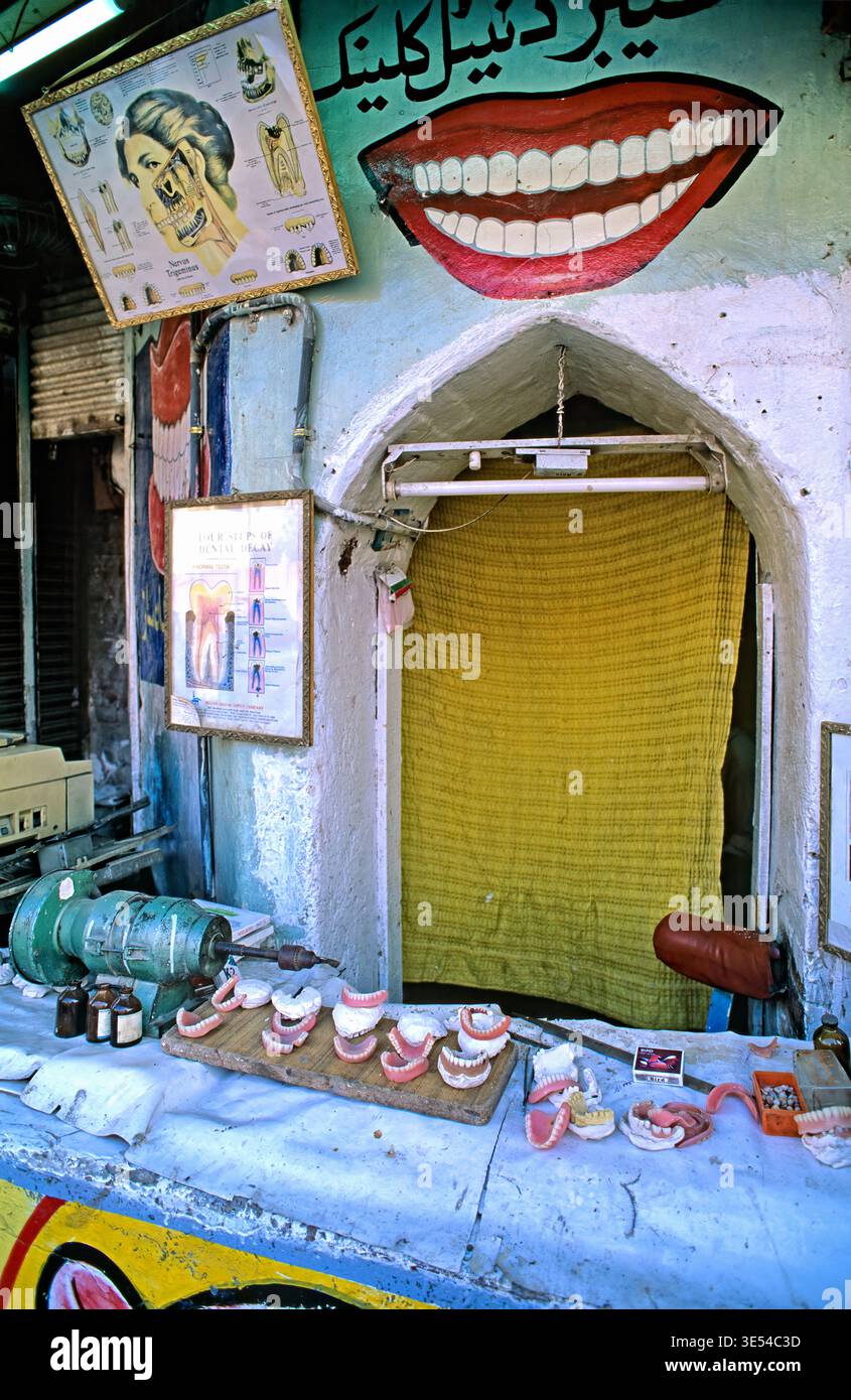 Un dentista di strada lavora a Peshawar. Gli strumenti e i modelli dentali sono visualizzati all'esterno. L'area e' colorata e trafficata. Foto Stock