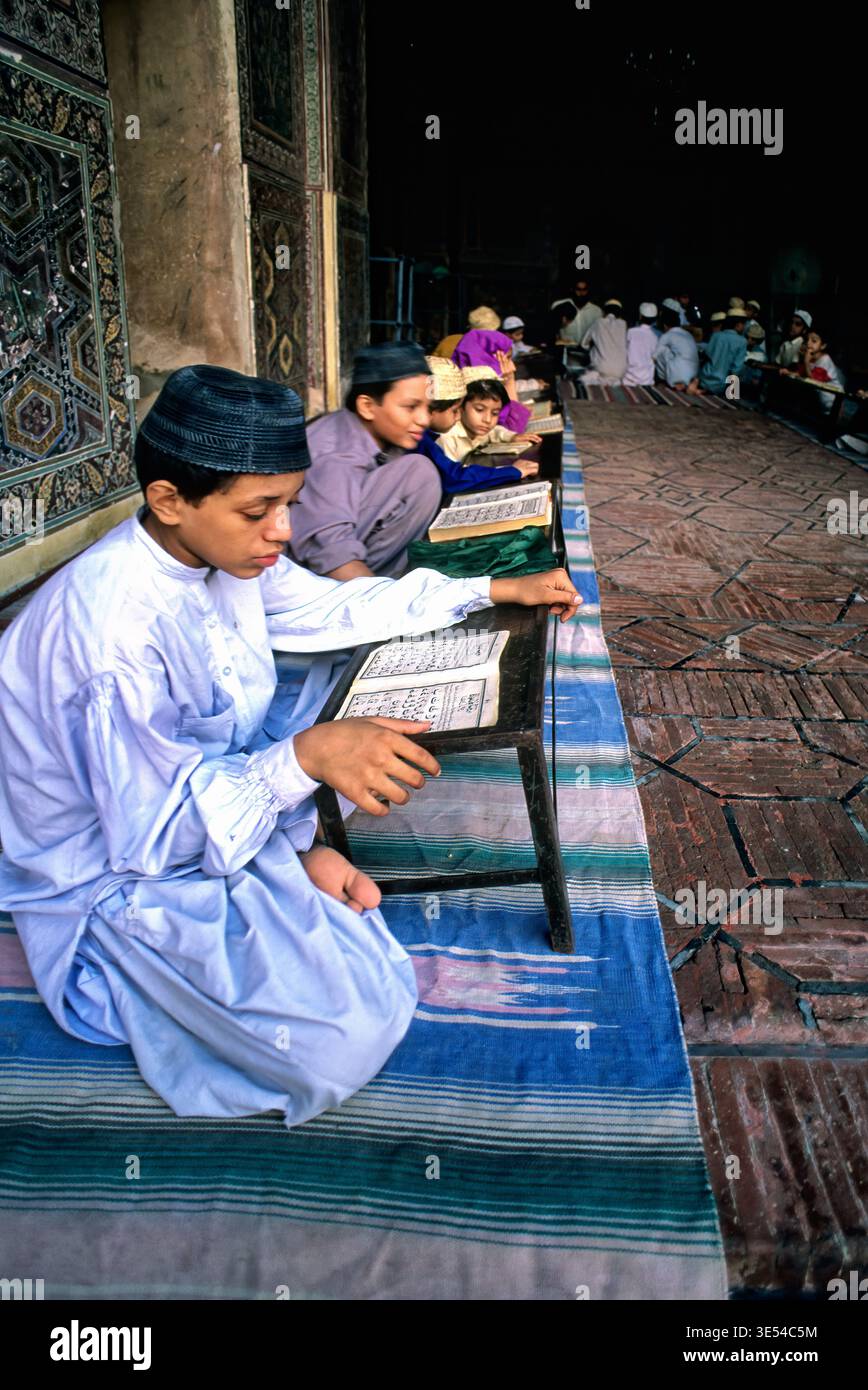Gli studenti si siedono sui tappetini leggendo e imparando in una scuola del Corano in Pakistan. L'impostazione mostra il coinvolgimento e la dedizione ai propri studi. Foto Stock
