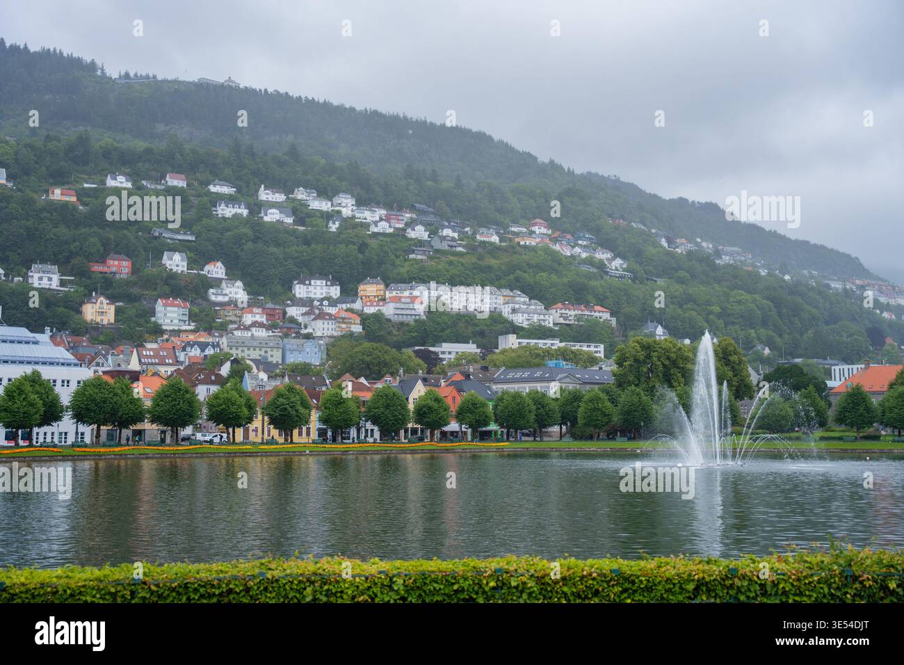 Bergen, Norvegia - 7 luglio 2024: Vista della fontana della città con montagne nebbiose ed edifici moderni. Foto Stock