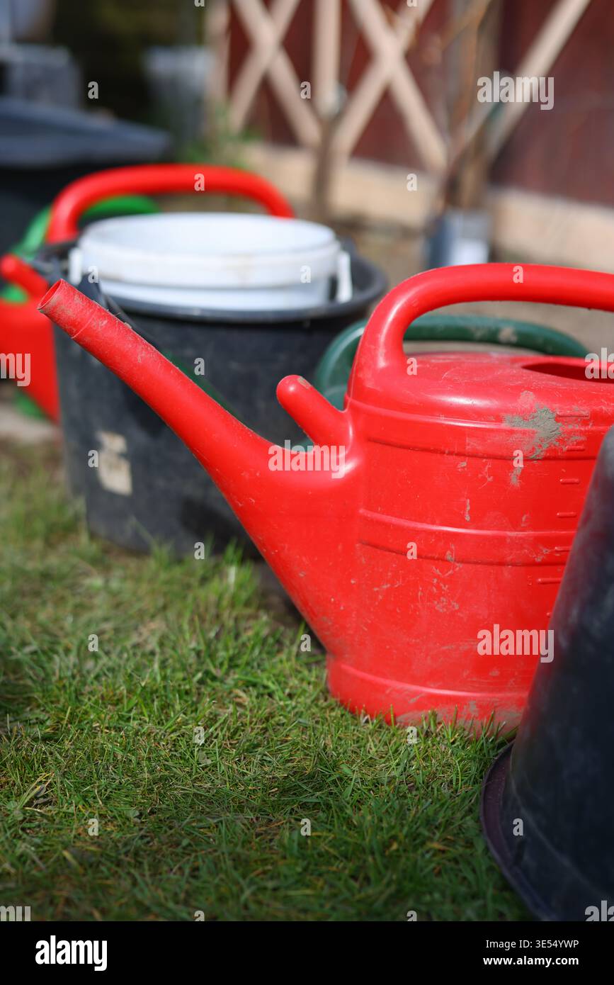 Annaffiatoi e secchi in plastica vicino al terreno, al giardinaggio primaverile e alla manutenzione del cortile. Foto Stock