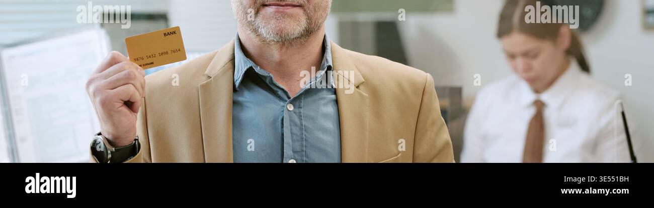 Intestazione dell'uomo caucasico di mezza età che tiene la carta bancaria all'interno della filiale della banca Foto Stock
