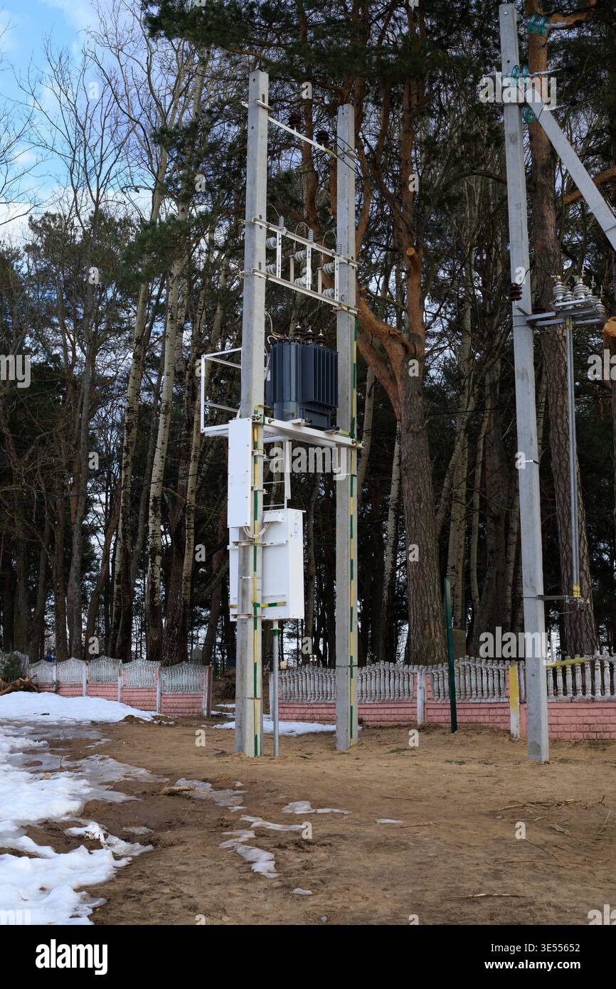 Sottostazione trasformatore elettrico per esterni su pali di cemento. Apparecchiature del sistema di distribuzione dell'energia elettrica situate in prossimità di un'area forestale per la fornitura di energia elettrica Foto Stock