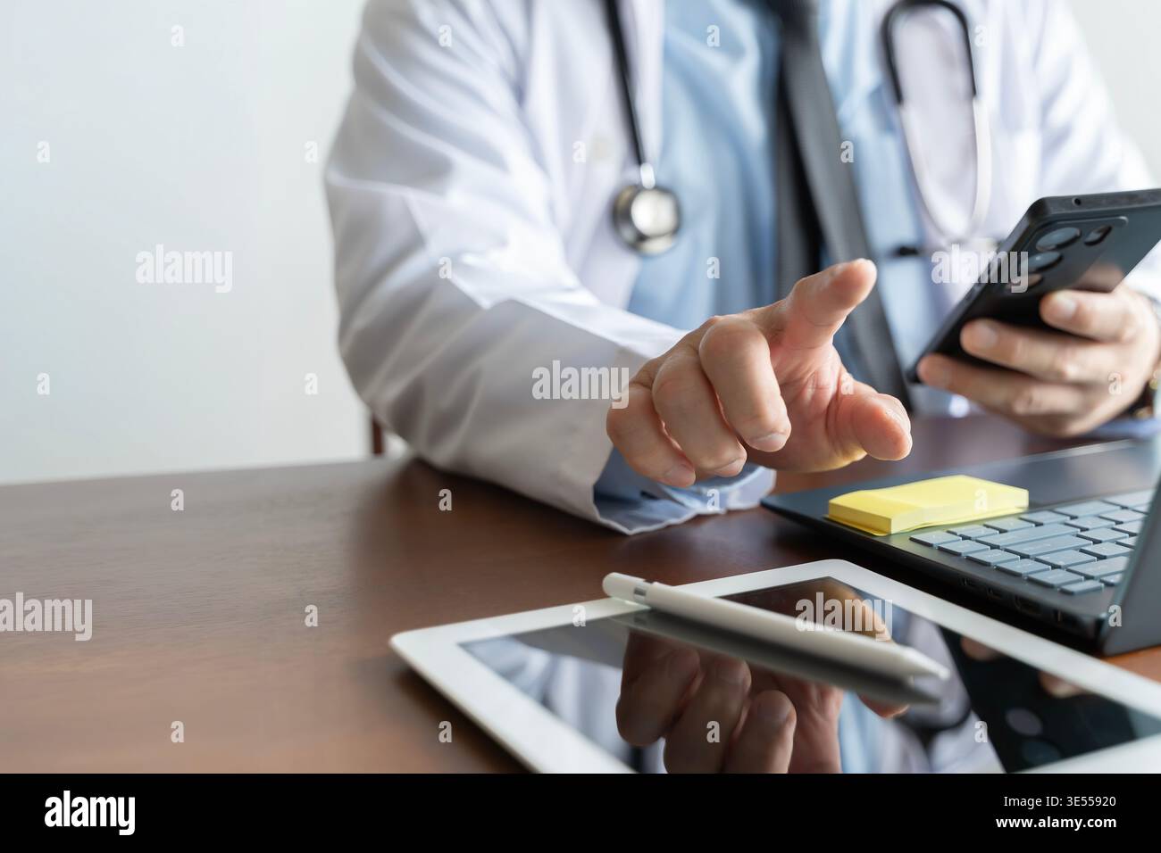 Medico che utilizza lo smartphone accanto a laptop e tablet in uno studio medico, illustrando la telemedicina, l'assistenza sanitaria mobile, la comunicazione digitale, i contro online Foto Stock