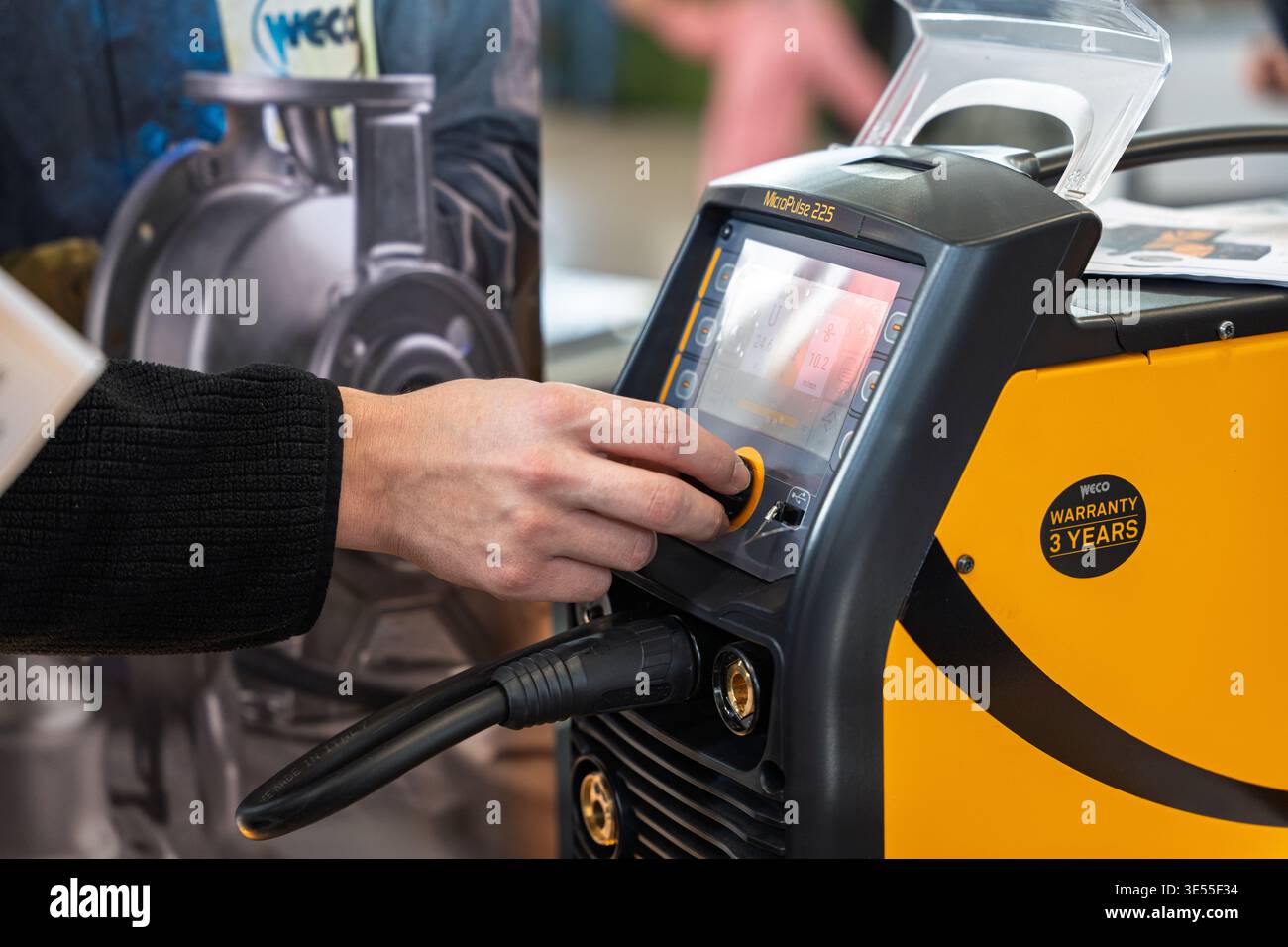 Primo piano di una persona che utilizza l'interfaccia digitale di una saldatrice professionale Weco MicroPulse 225 in una fiera, evidenziando le caratteristiche avanzate Foto Stock
