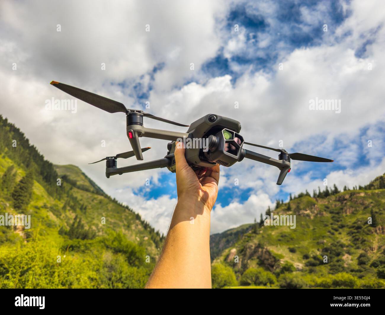 Un uomo adulto tiene il drone su un terreno montuoso, circondato da un paesaggio verde. Il cielo nuvoloso migliora l'umore di attesa e avventura durante l'esplorazione. Foto Stock