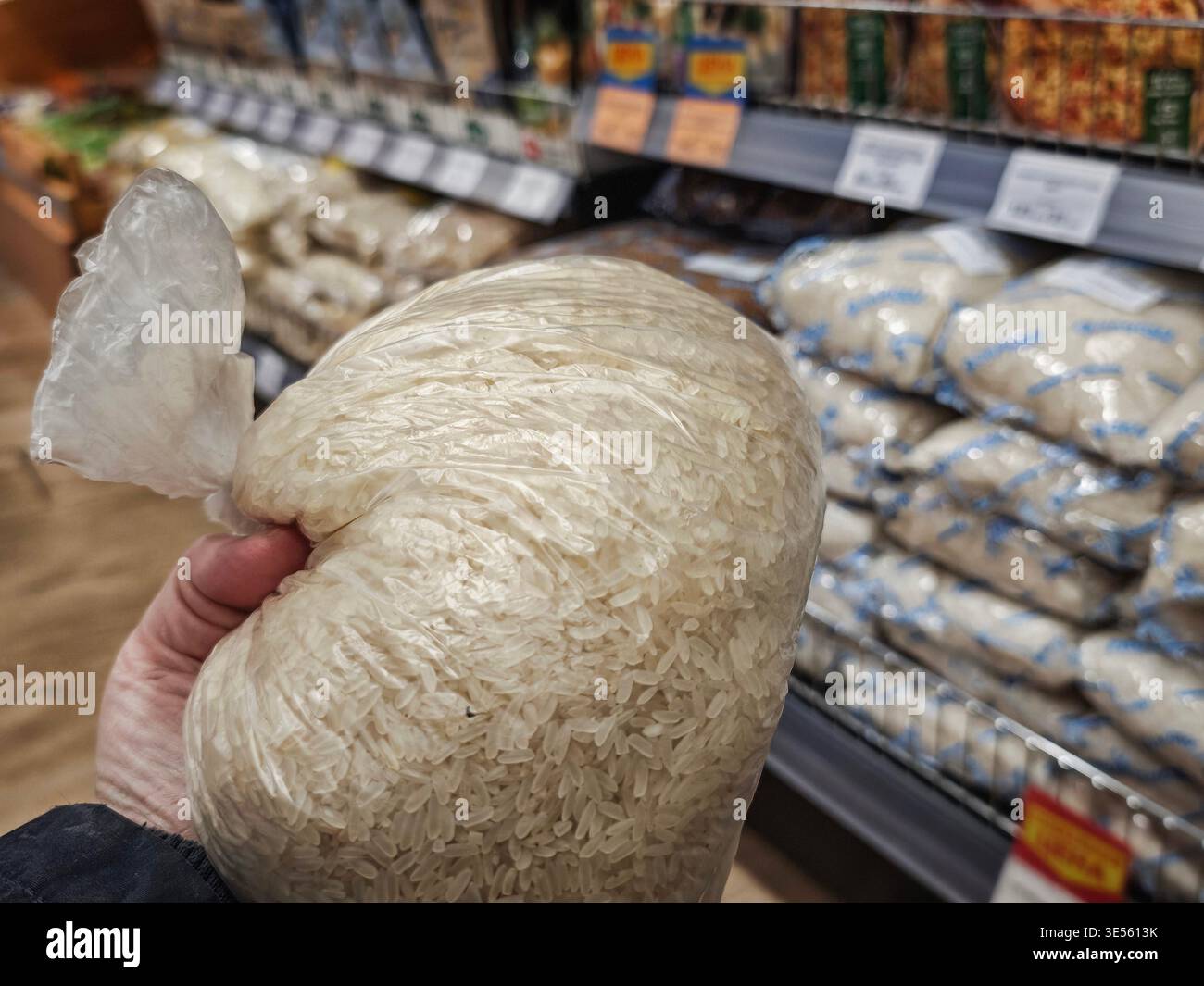Una mano sta tenendo un sacchetto di riso in un negozio di alimentari, selezionandolo dallo scaffale tra i vari prodotti alimentari disponibili per l'acquisto. Foto Stock