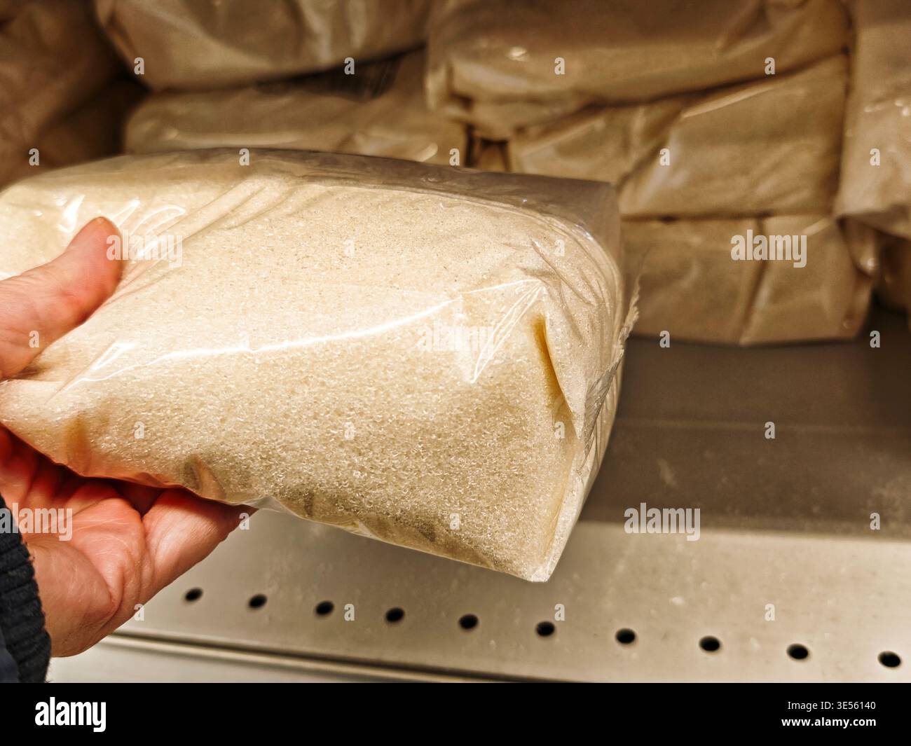 Un cliente sceglie una confezione di zucchero dagli scaffali di un negozio di alimentari riempita con diversi prodotti per le esigenze quotidiane Foto Stock