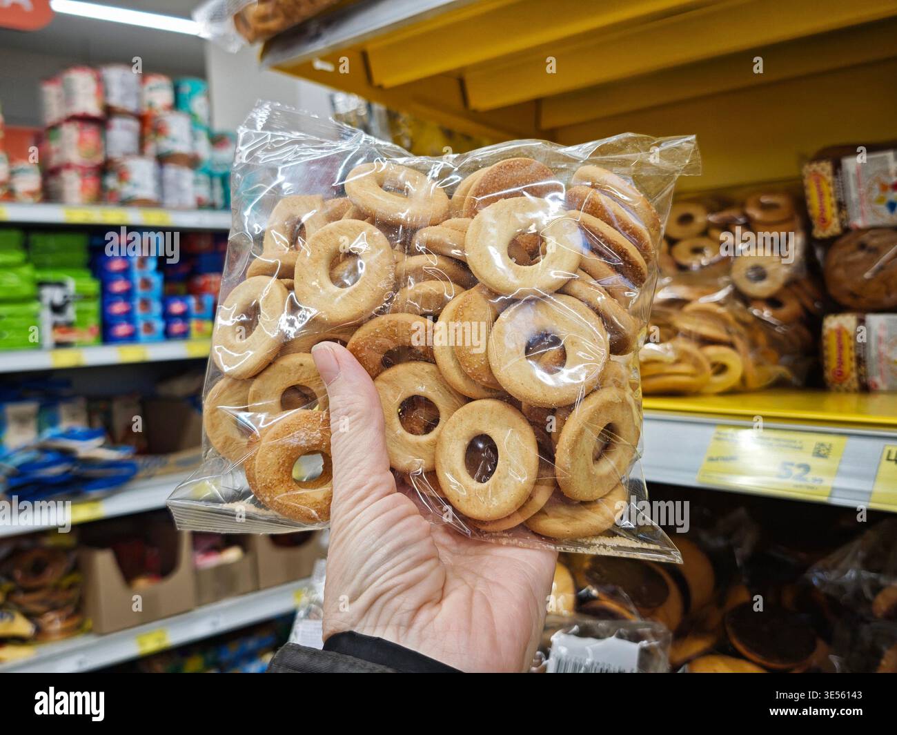 Una persona tiene in mano una borsa di biscotti mentre fa acquisti in un negozio di alimentari. Gli scaffali sono pieni di vari prodotti alimentari. Foto Stock