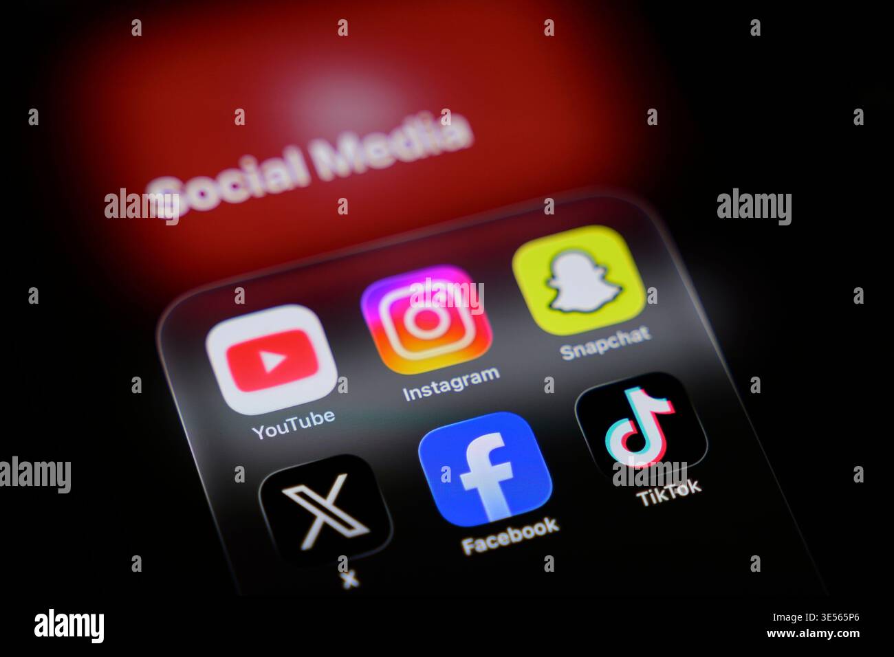 Schermo dello smartphone con cartella dell'app "Social Media" (YouTube, Instagram, Snapchat, X, Facebook, TikTok) e logo YouTube sfocato dietro. Foto Stock
