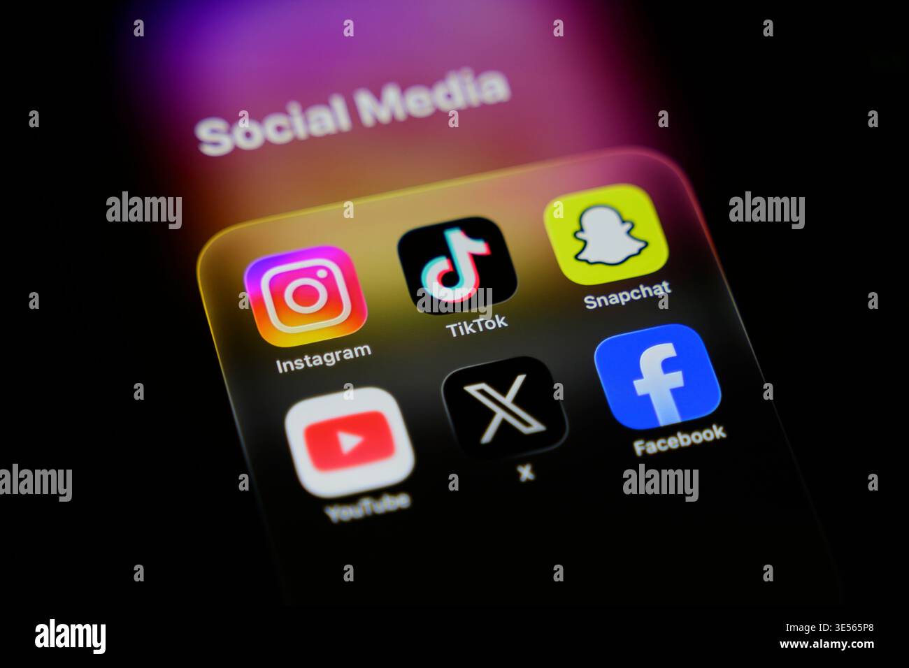 Schermata dell'iPhone che mostra la cartella dell'app "Social Media" (Instagram, TikTok, Snapchat, YouTube, X, Facebook) e un logo Instagram sfocato Foto Stock