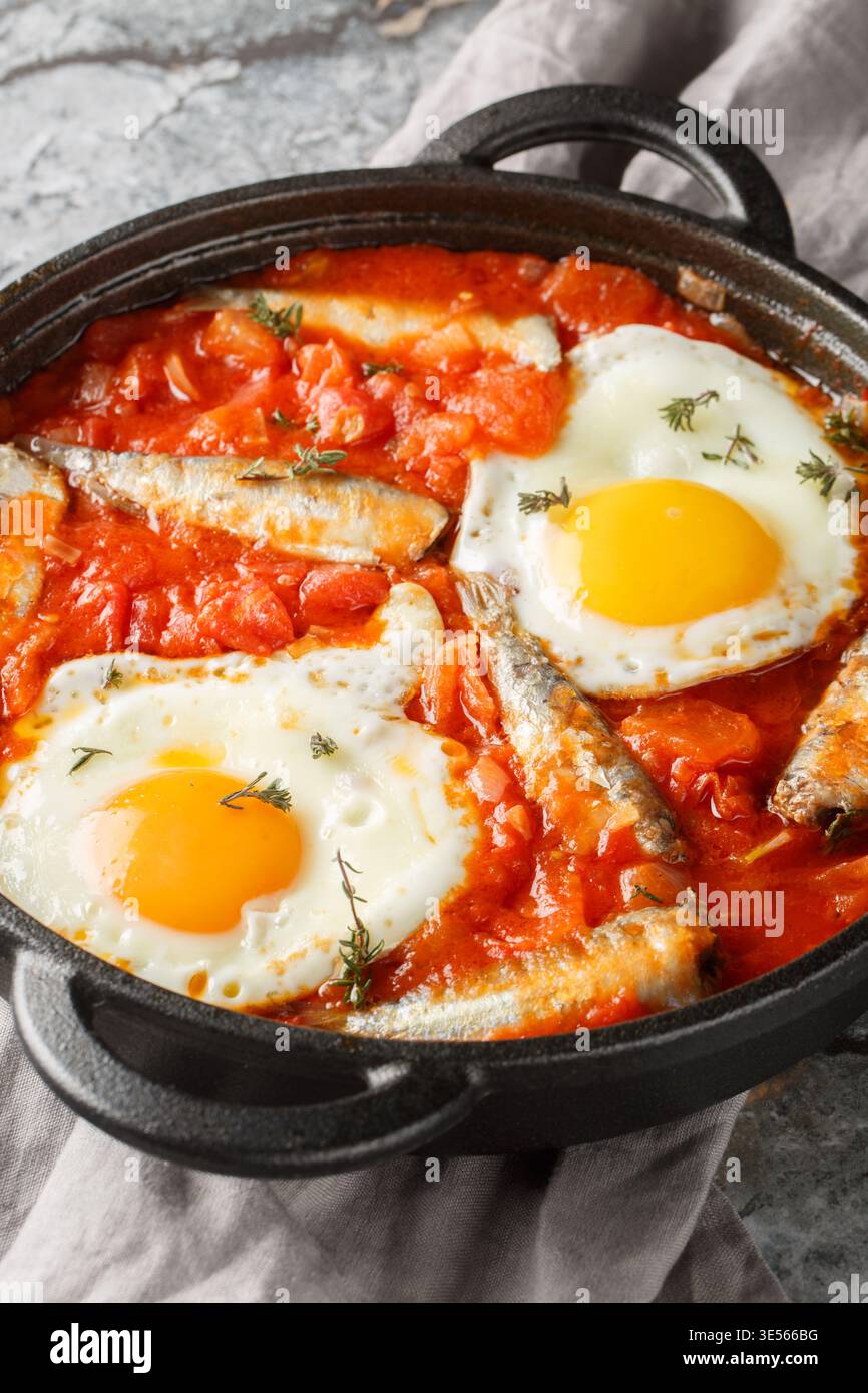 Uova fritte con sardine in scatola e verdure sospese in salsa di pomodoro da vicino in una padella sul tavolo. Verticale Foto Stock